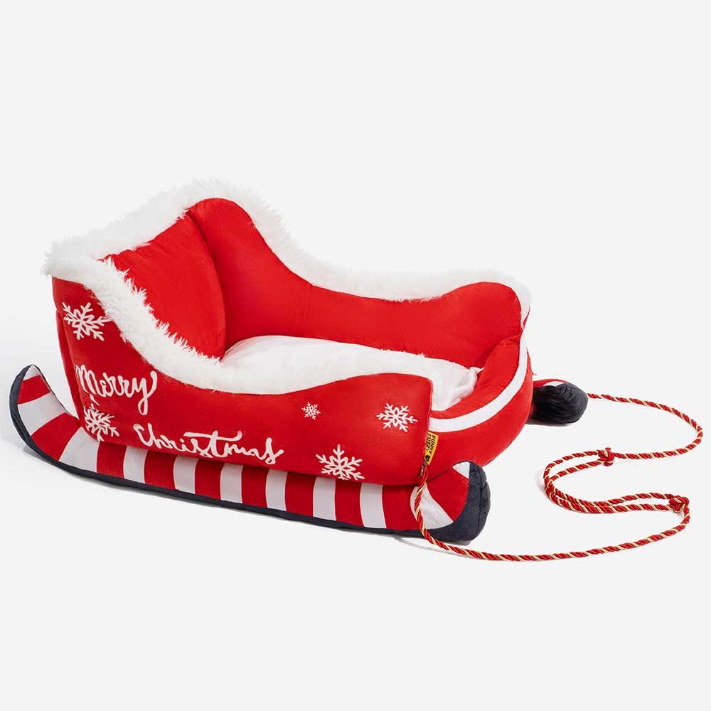 Christmas-themed dog bed in sleigh design featuring soft red fabric and decorative rope accents.
